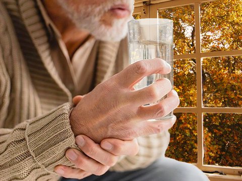 Старый мужчина с болезнью Паркинсона со стаканом воды у окна